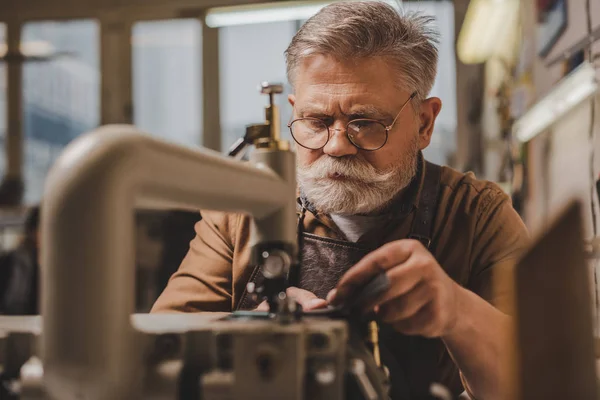 Selective focus of senior shoemaker near sewing machine in workshop — Stock Photo