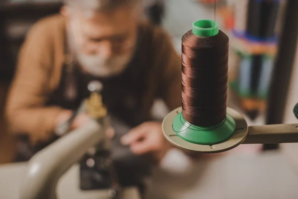 Selektiver Fokus der Spule mit Fäden in der Nähe des Schuhmachers, der an der Nähmaschine arbeitet — Stockfoto