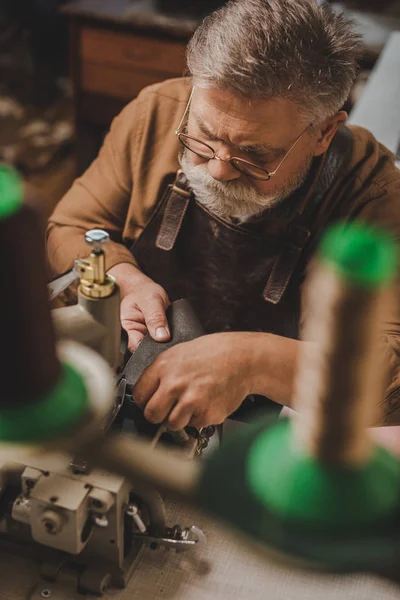Selective focus of senior shoemaker sewing leather on sewing machine in workshop — Stock Photo