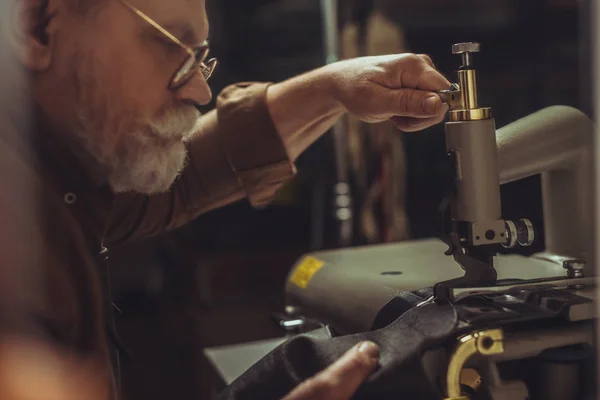 Selective focus of senior cobbler sewing genuine leather on sewing machine in workshop — Stock Photo