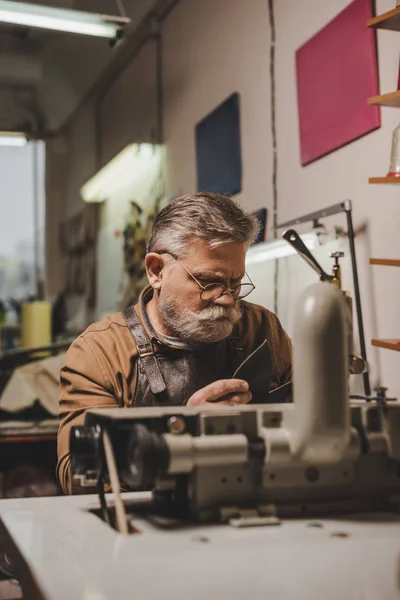 Selective focus of senior shoemaker sewing leather on sewing machine in workshop — Stock Photo