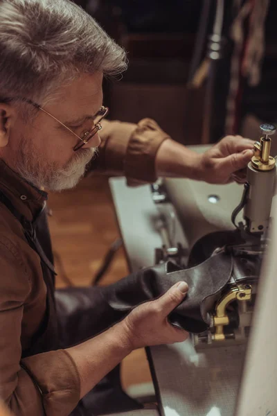 Foco seletivo de couro de costura sapateiro sênior na máquina de costura na oficina — Fotografia de Stock