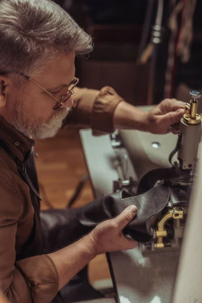 Selective focus of senior cobbler sewing leather on sewing machine in workshop — Stock Photo