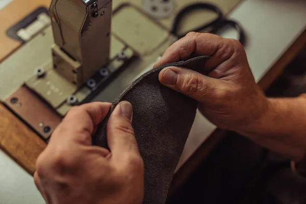 Vista parcial del zapatero que sostiene la pieza de cuero genuino cerca de la máquina de coser - foto de stock