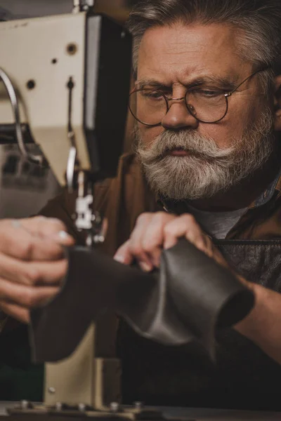 Selective focus of attentive, senior shoemaker sewing leather on sewing machine — Stock Photo