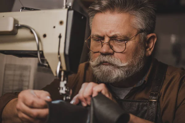 Senior, bearded cobbler sewing leather on sewing machine — Stock Photo