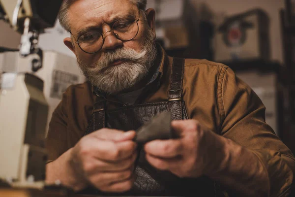 Selective focus of attentive cobbler looking at piece of genuine leather — Stock Photo