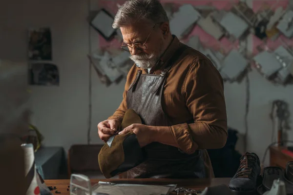 Selective focus of senior cobbler holding piece of genuine leather in workshop — Stock Photo