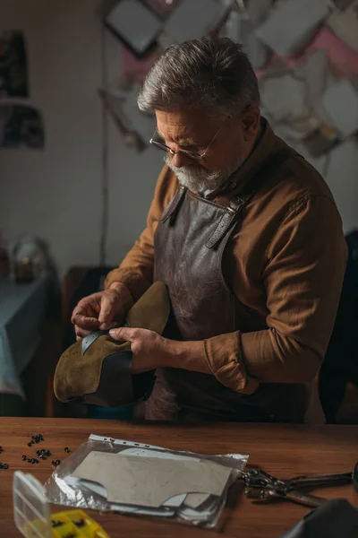 Oberschuster in Schürze hält Stück echtes Leder in Werkstatt — Stockfoto