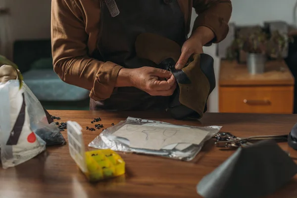Cropped view of cobbler holding piece of leather near desk with tools — Stock Photo