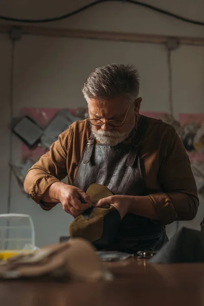 Selective focus of senior cobbler holding piece of genuine leather in workshop — Stock Photo