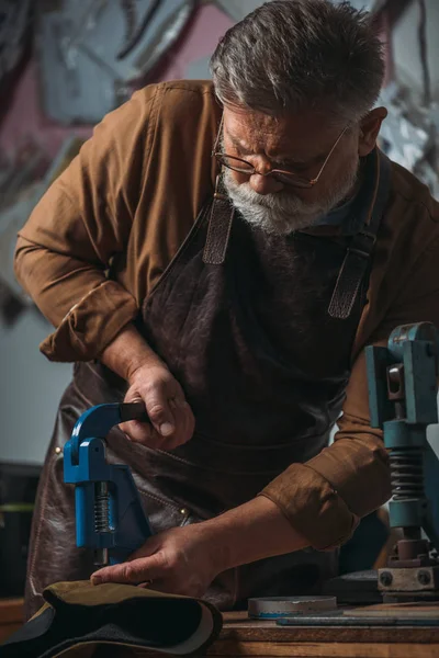Sapateiro sênior fazendo buracos em couro com puncher — Fotografia de Stock