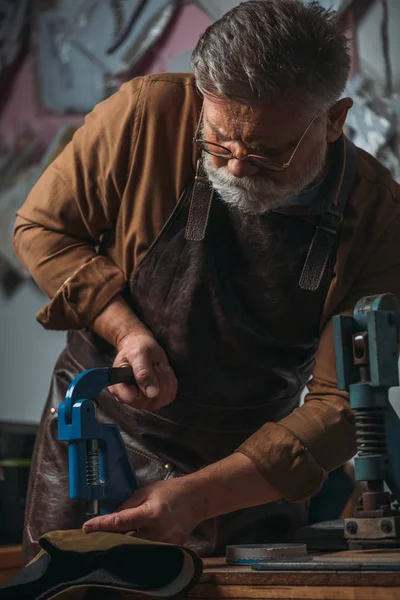 Zapatero senior haciendo agujeros en cuero con perforador — Stock Photo