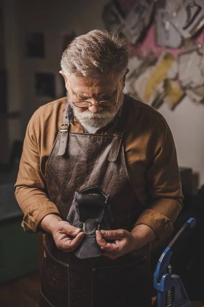 Attentive, senior cobbler holding leather detail in workshop — Stock Photo