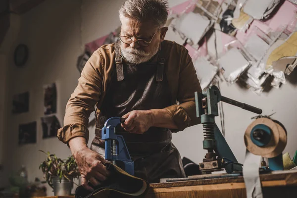 Calzolaio senior che fa buchi in pelle con puncher — Foto stock