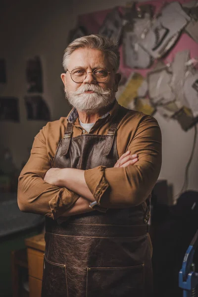 Smiling, bearded cobbler standing with crossed arms and looking at camera — Stock Photo