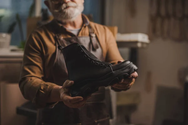 Foco seletivo de sapateiro mostrando bota de couro artesanal na oficina — Fotografia de Stock