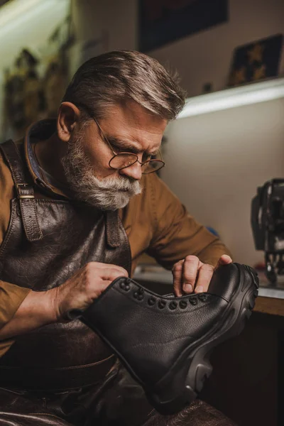 Attentive, senior shoemaker holding leather boot in workshop — Stock Photo