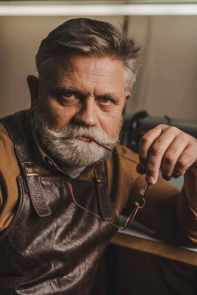 Senior, confident cobbler looking at camera while holding glasses — Stock Photo