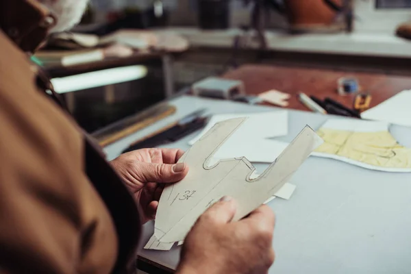Обрезанный вид сапожника с бумажным шаблоном в мастерской — стоковое фото