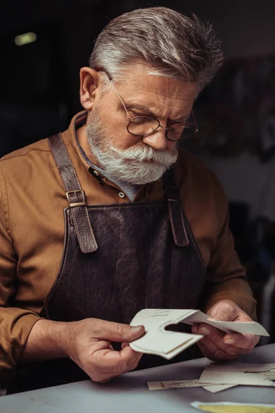 Senior, aufmerksamer Schuster hält Papierschablone in Werkstatt — Stockfoto