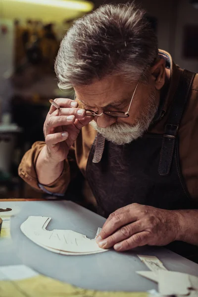 Cordonnier attentif touchant lunettes tout en regardant modèle dans l'atelier — Photo de stock