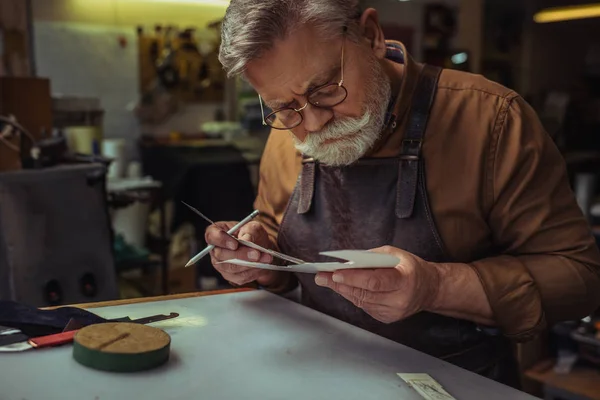 Focused, bearder shoemaker looking at paper template in workshop — Stock Photo