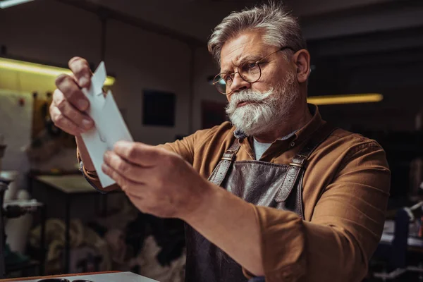 Senior, attentive cobbler looking at template in workshop — Stock Photo