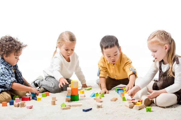 Mignons enfants multiethniques jouant avec des blocs de bois sur le tapis, isolé sur blanc — Photo de stock