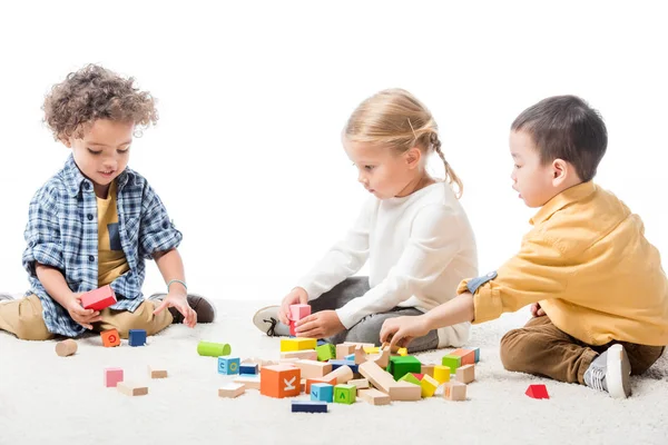 Crianças multiculturais brincando com blocos de madeira no tapete, isolado em branco — Fotografia de Stock