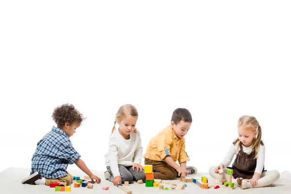 Enfants multiculturels jouant avec des blocs de bois sur le tapis, isolé sur blanc — Photo de stock