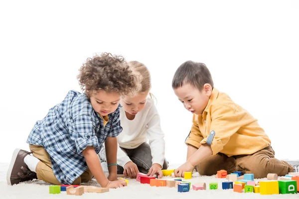 Enfants multiethniques jouant avec des blocs de bois sur le tapis, isolés sur le blanc — Photo de stock