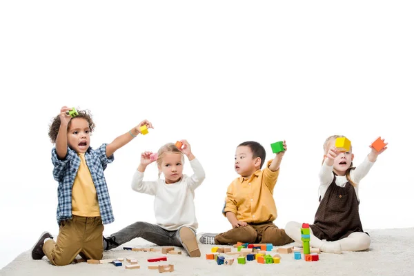 Enfants multiculturels émotionnels jouant avec des blocs de bois sur le tapis, isolé sur blanc — Photo de stock