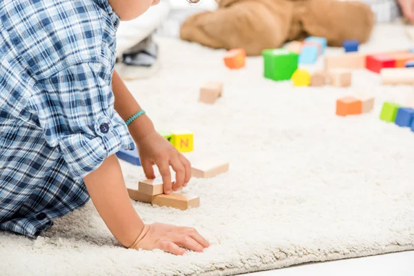 Cropped view of kids playing with wooden blocks on carpet — Stock Photo