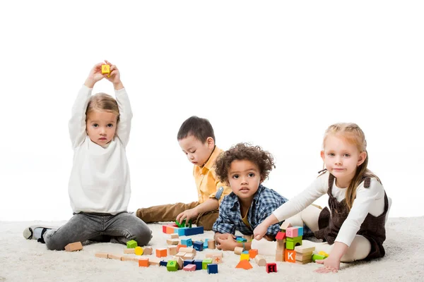 Очаровательные многонациональные дети, играющие с деревянными блоками на ковре, изолированные на белом — стоковое фото