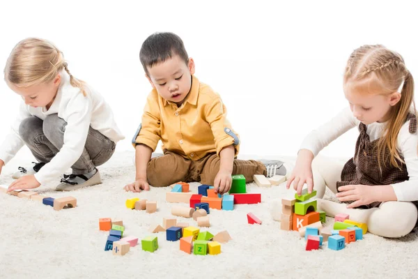 Multikulturelle Kinder spielen mit Holzklötzen auf Teppich, isoliert auf Weiß — Stockfoto