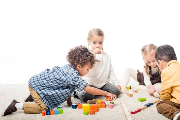 Мультикультурні діти грають з дерев'яними блоками на килимі, ізольовані на білому — стокове фото