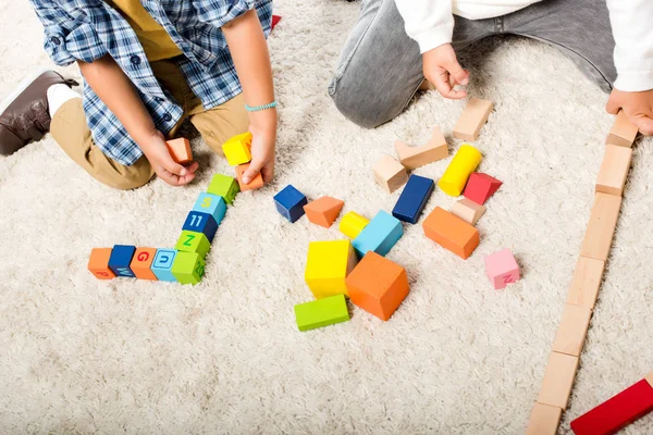 Cropped view of kids playing with wooden blocks on carpet — Stock Photo