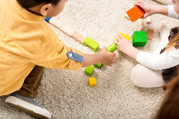 Cropped view of kids playing with colorful wooden blocks on carpet — Stock Photo