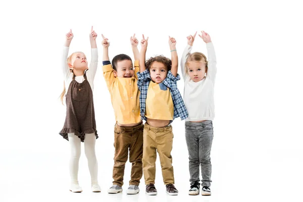 Niños alegres multiétnicos jugando y apuntando hacia arriba aislados en blanco - foto de stock