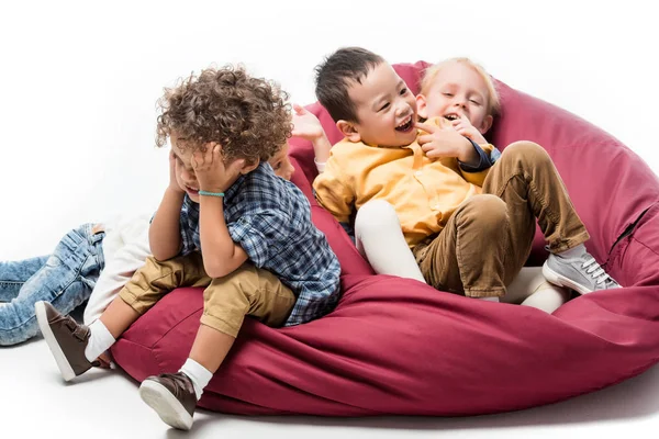 Niños multiculturales jugando juntos en la silla de la bolsa de basura roja en blanco - foto de stock