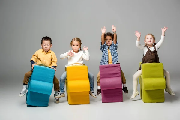 Adorable multicultural kids playing and sitting on puzzles on grey — Stock Photo