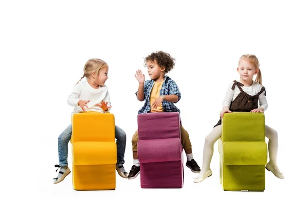 Multiethnische Kinder sitzen auf Puzzlestühlen, isoliert auf weiß — Stockfoto