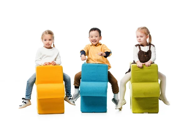 Enfants multiethniques assis sur des chaises de puzzle, isolé sur blanc — Photo de stock