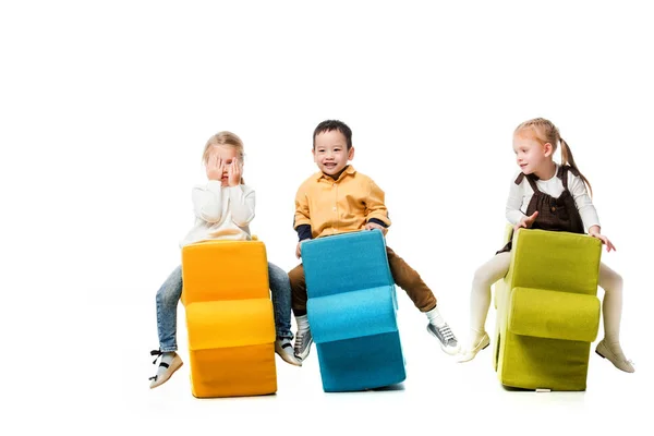 Веселі мультикультурні діти сидять на стільцях-головоломках, ізольовані на білому — стокове фото