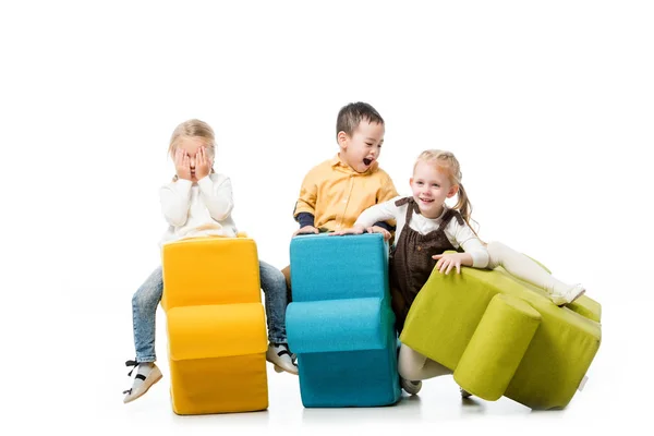 Cheerful multicultural children sitting on puzzle chairs, on white — Stock Photo
