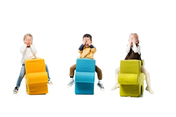 Multikulturelle Kinder, die die Augen schließen und auf Puzzlestühlen sitzen, isoliert auf weiß — Stockfoto