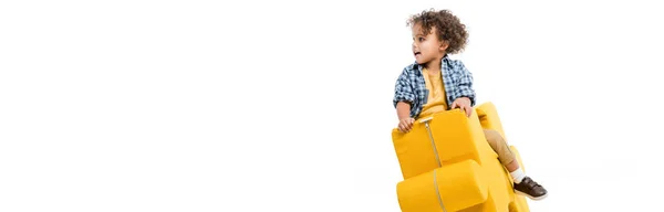 Tiro panorâmico de pequeno menino afro-americano sentado em cadeira de quebra-cabeça amarelo, isolado em branco — Fotografia de Stock