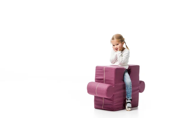 Задумчивый ребенок сидит на фиолетовом стуле головоломки, изолированный на белом — стоковое фото
