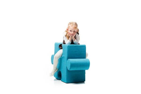 Bored kid sitting on blue puzzle chair, isolated on white — Stock Photo